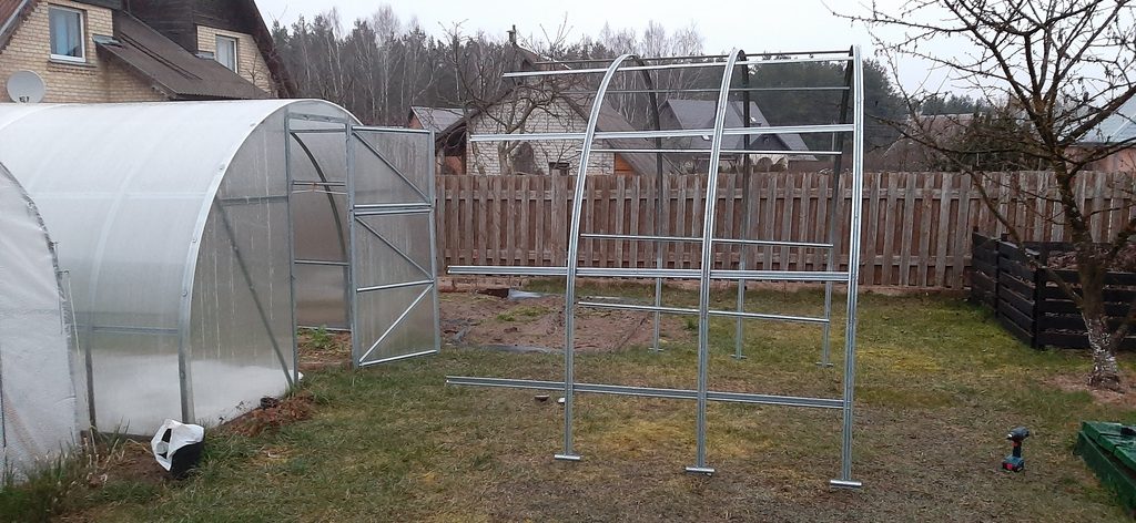 Greenhouse extension frame standing next to existing greenhouse
