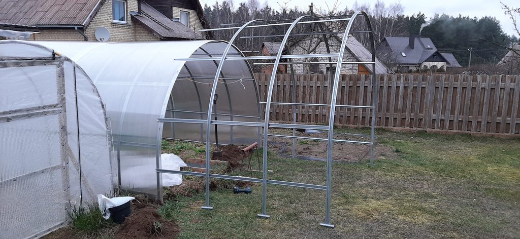 New greenhouse extension frame positioned beside existing polycarbonate greenhouse