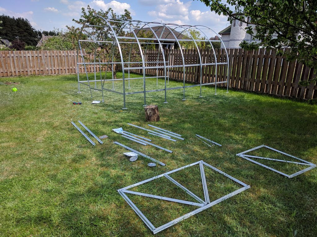 Partly assembled greenhouse door sections laid on the grass in front of the main frame.
