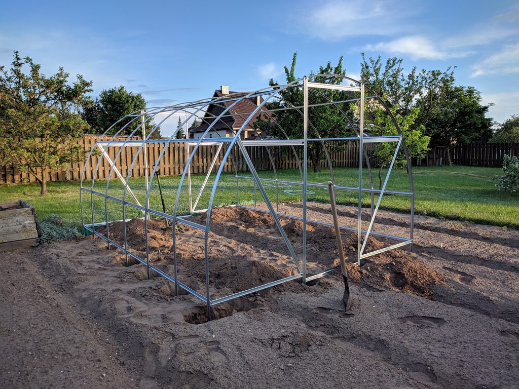 Angled view of the greenhouse frame showing its lower legs positioned in holes in the soil.
